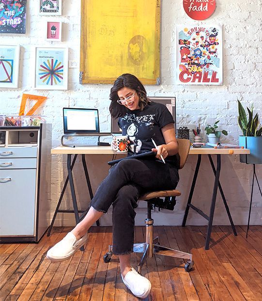 A photo of Maïa Faddoul sitting on a chair, in front of her desk in her wokrspace.